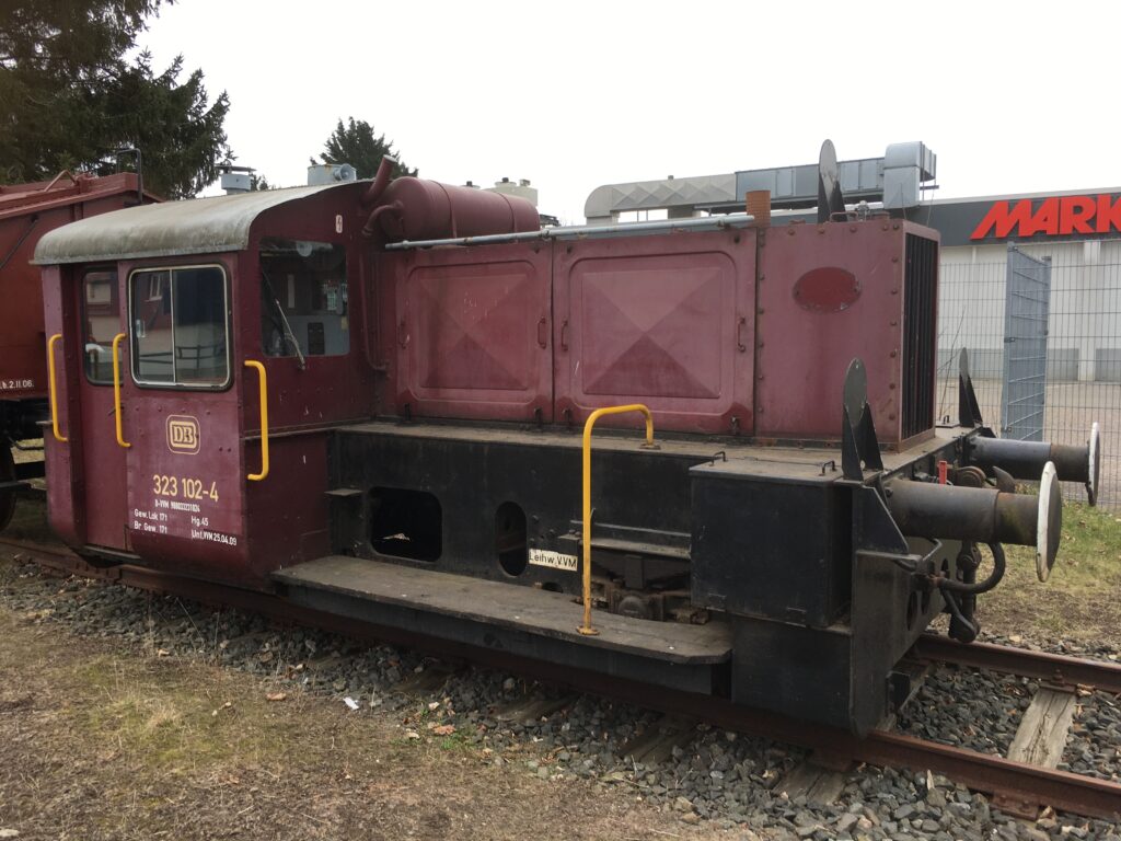 Die kleine rote Diesel Rangierlok der DB mit gelben Haltegriffen und schwarzem Fahrwerk. Das Gehäuse vom Motor und Fahrhaus ist weinrot.