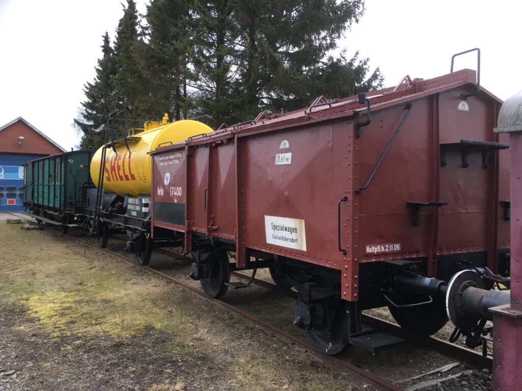 Vorn ein brauner Güterwagen mit Deckel-Dach, dann ein Kesselwaggon in gelb mit roter Schrift SHELL und zuletzt ein kleiner grüner Waggon aus Holz.