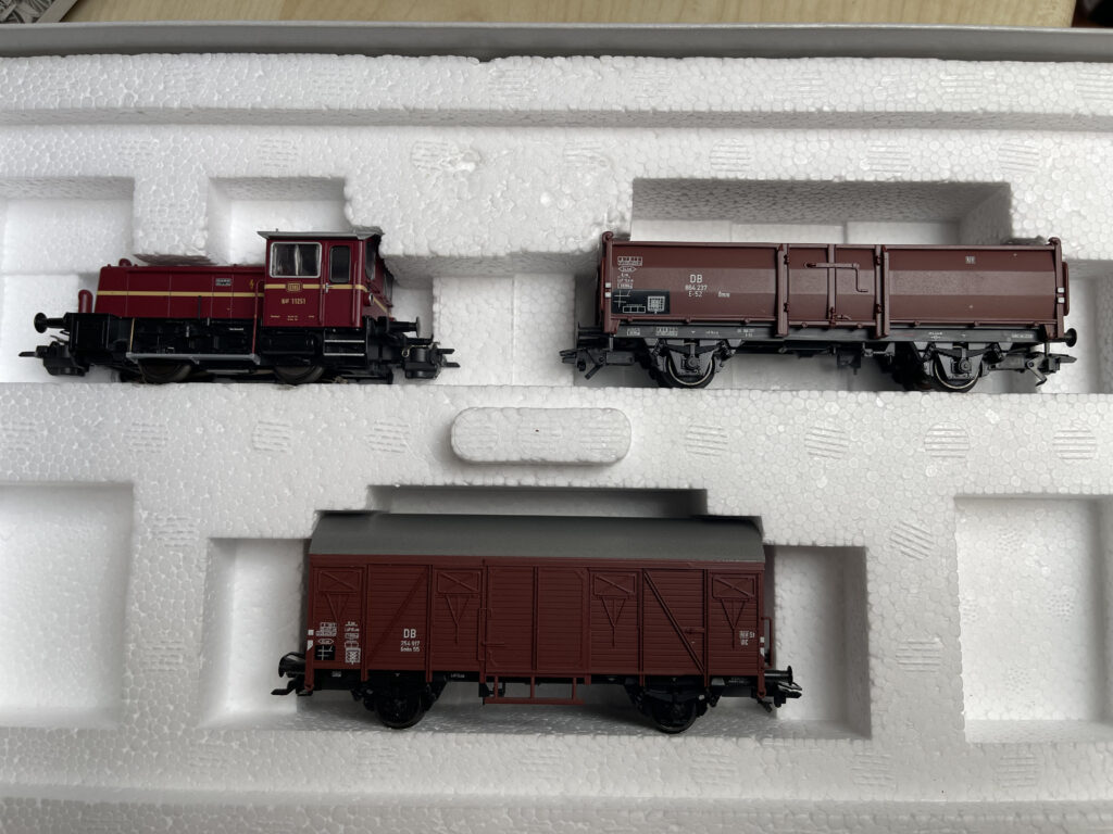 Die offene Packung. Oben links die weinrote Köf III. Eine kleine Diesel Rangierlok. Daneben der braune offene Güterwagen.
Da drunter der braune geschlossene Güterwagen.