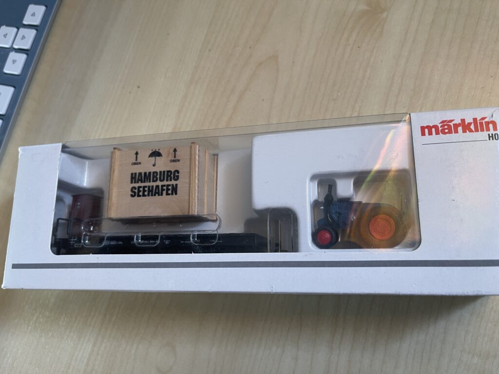 In der weißen Packung der Flachwagen, die hellbraune Holzkiste mit Aufschrift "Hamburg Seehafen" und Pfeilen für "Oben" und Regenschirm.
Dann der blaue Lanz Bulldog Traktor mit roten Felgen.
Alles noch unter der durchsichtigen Pastikhülle.