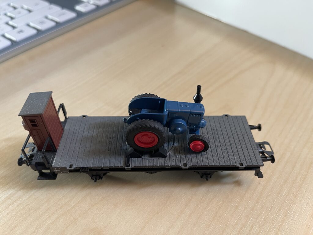Der blaue Lanz Bulldog Traktor steht allein auf dem schwarzen Flachwagen mit braunem Bremserhäuschen.