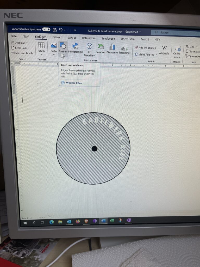 Foto vom Bildschirm auf dem Word mit einem Zeichenobjekt Kreis zu sehen. Im Kreis steht "Kabelwerk Kiel".
Mittig ist ein schwarzer Punkt.
