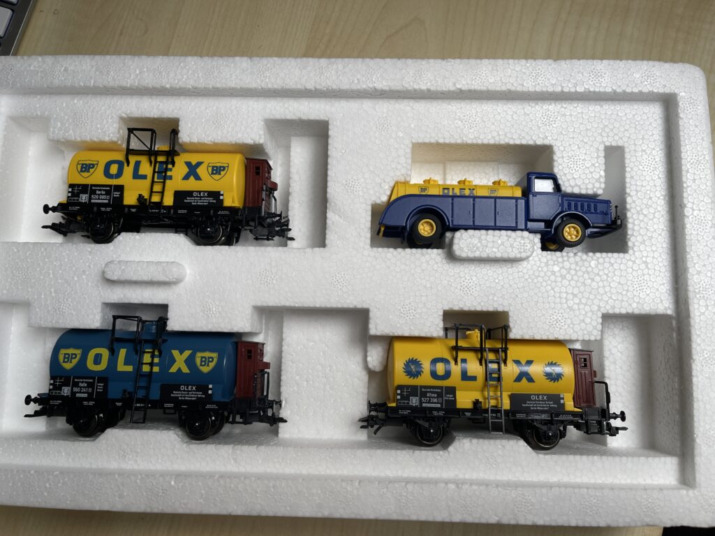 Die geöffnete Packung zeigt die drei Kesselwagen. Zwei in gelb mit blauer Aufschrift Olex und ein Wagen in blau mit gelber Aufschrift.
Der Tankwagen ist ein blauer LKW mit gelbem Tank auf der Ladefläche.
