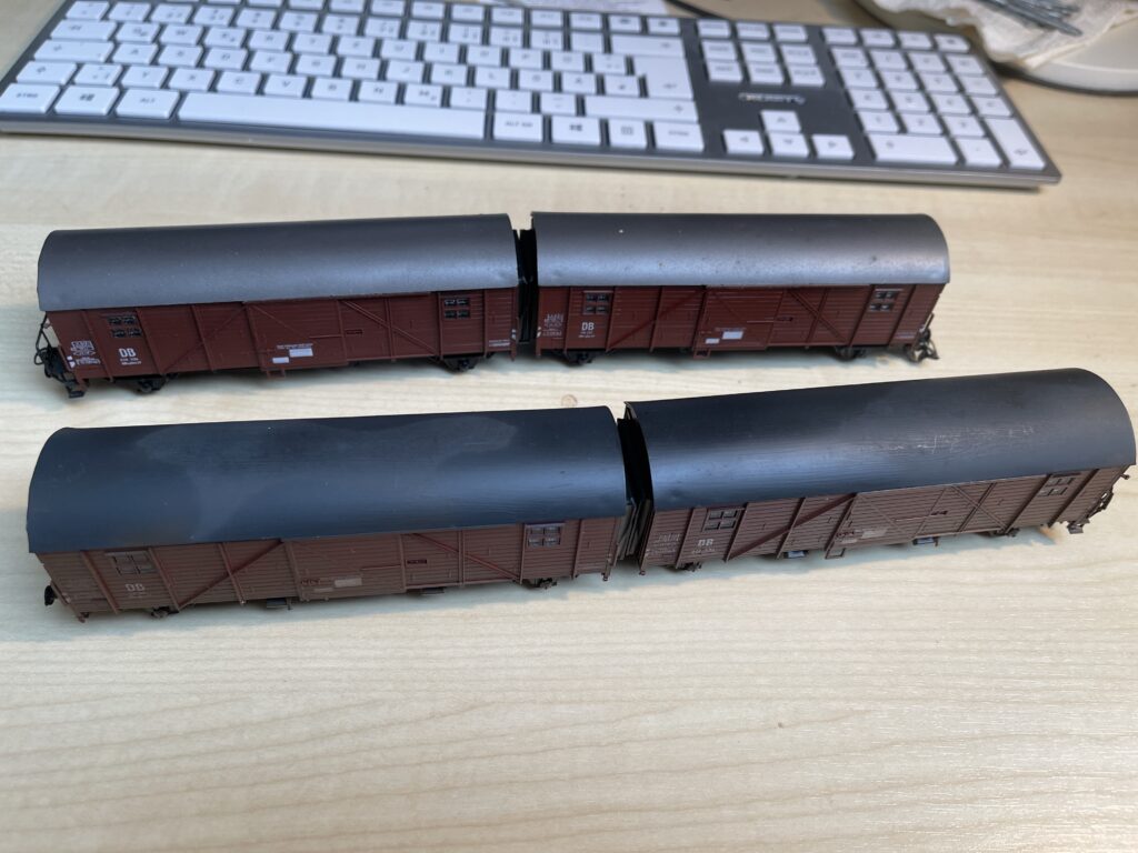 Auf dem hellen Schreibtisch stehen die zwei Leig-Einheiten.
Es sind je zwei Güterwagen mit grauem Blechdach und Holzwänden zu einer Einheit verbunden.