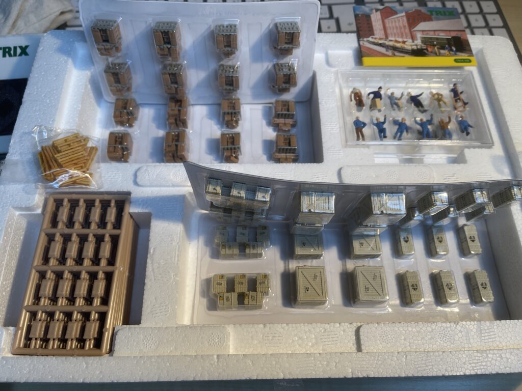 Die offene Packung. Zu sehen sind ein Tütchen Paletten, viele Spritzguss Rahmen mit Säcken. Kleine und große Kisten, eine Packung Männchen. Unten noch einige hellere Kisten.