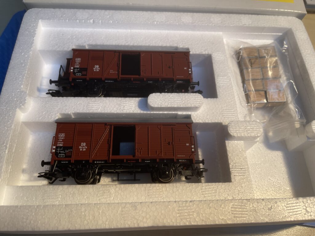 Die offene Packung mit zwei braunen Güterwagen und Holzkisten deren Ränder mit Metall Bändern verstärkt sind. Typische Teekisten.