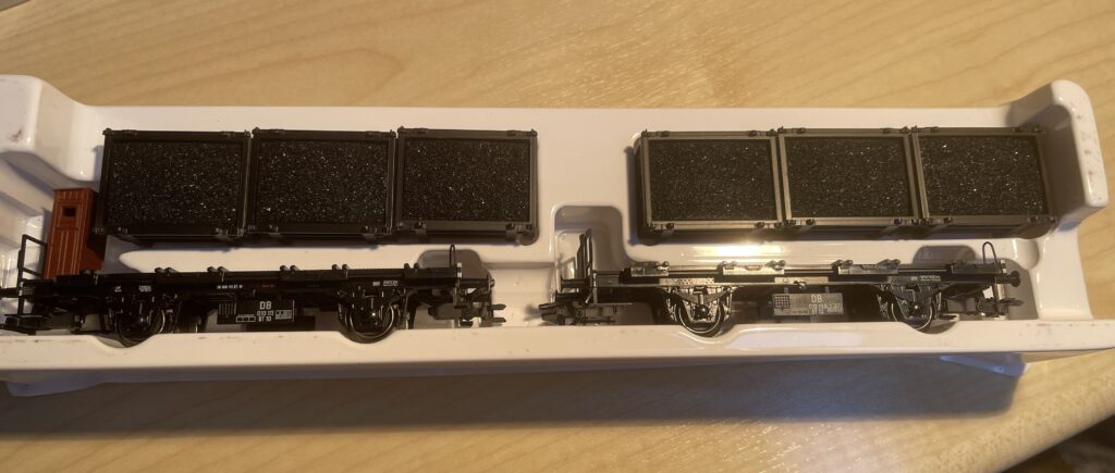 Die schmale weiße Plastikhalterung hält die zwei Flachwagen. Darüber sind vier schwarze Kästen mit Kohle zu sehen.
